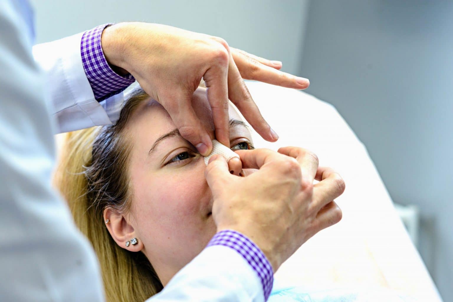 Doctor examining the nose of a female patient for a nasal fracture.